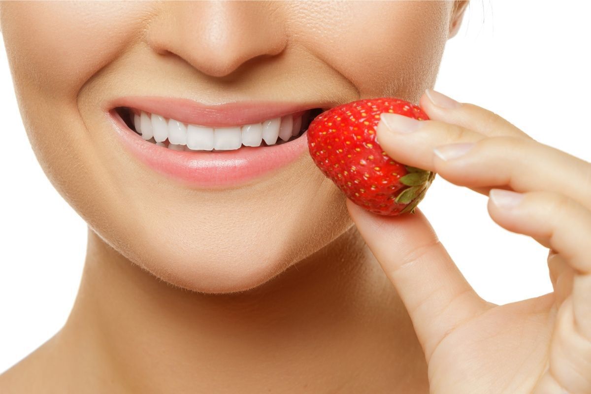 Woman smiling while eating a fresh strawberry, demonstrating tooth-friendly foods for dental health.