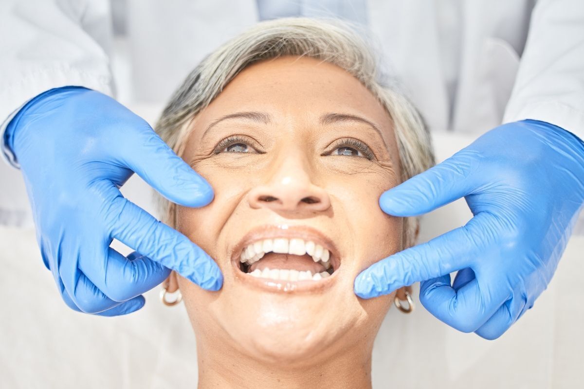Mature patient smiling while dentist examines teeth during oral health consultation.